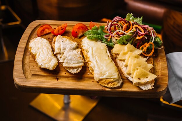 Vista superior, um homem segura uma bandeja com torradas de queijo com fatias de tomate e salada de legumes