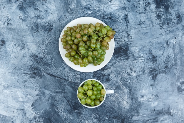 Vista superior uvas verdes em chapa branca e copo em fundo de gesso sujo. horizontal