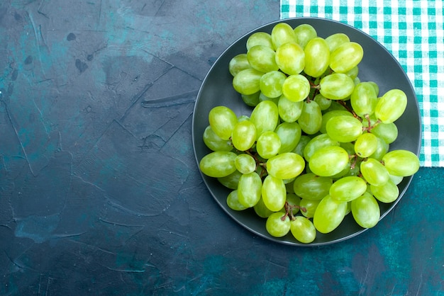Vista superior uvas verdes frescas frutas maduras e suculentas dentro do prato na mesa azul escura.