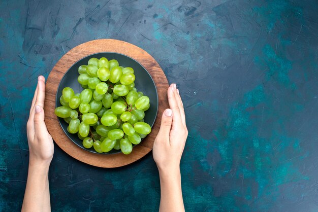 Vista superior uvas verdes frescas frutas maduras e suculentas dentro do prato na mesa azul escura.