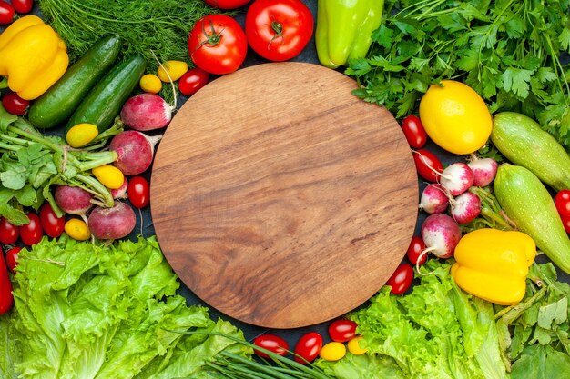 Vista superior vegetais frescos tomates alface rabanete limão abobrinha salsa tomate cereja tábua redonda de madeira no centro na superfície escura