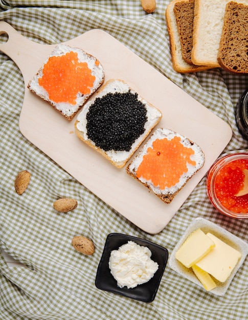 Foto grátis vista superior vermelho e preto caviar torrada centeio e pão branco com queijo cottage caviar vermelho caviar preto e amêndoa em cima da mesa