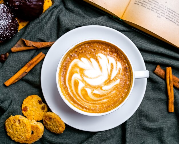 Vista superior xícara de cappuccino com biscoitos e um livro na mesa