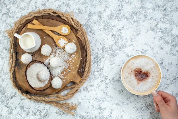 Foto grátis vista superior xícara de cappuccino na tigela de pó de coco de mãos femininas bolas de coco colheres de tigela de leite na placa de madeira na superfície cinza