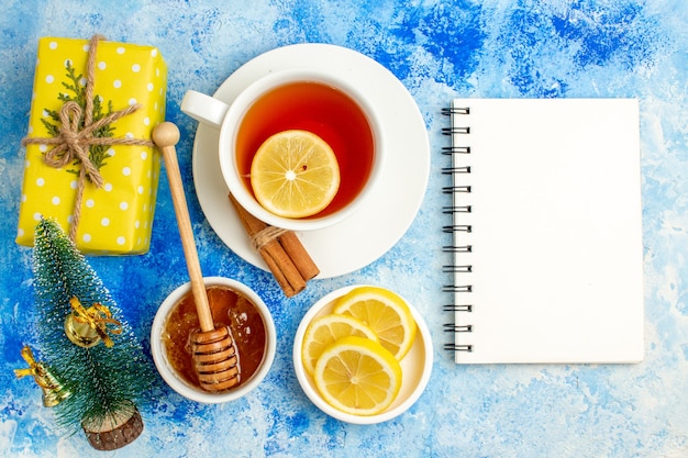 Vista superior xícara de chá amarelo caixa de presente mel fatias de limão pequeno bloco de notas de árvore de natal na mesa azul
