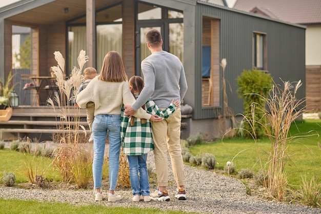 Vista traseira da família abraçando e admirando sua casa