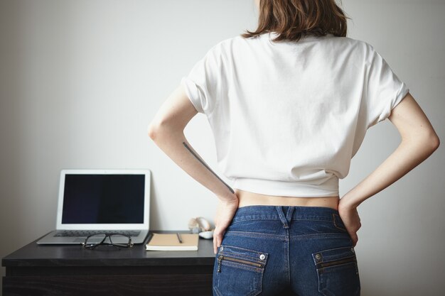 Vista traseira da garota hippie vestindo jeans e camiseta branca em branco com copyspace para seu texto ou conteúdo promocional dentro de casa. Pessoas, estilo, moda, tecnologia moderna e conceito de design de roupas