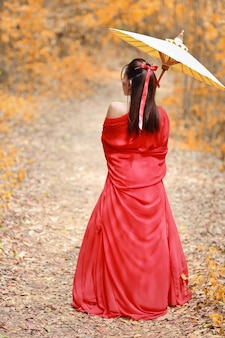 Vista traseira da linda mulher asiática em traje chinês guerreiro vermelho com guarda-chuva antiga