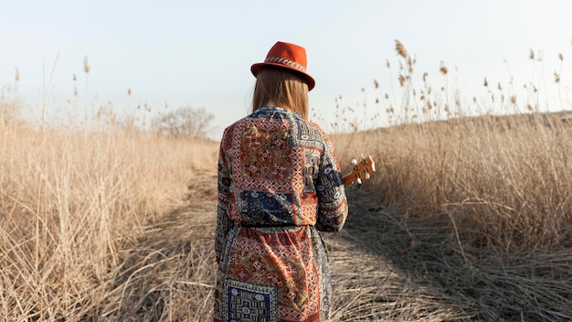 Vista traseira da mulher boêmia com ukulele na natureza