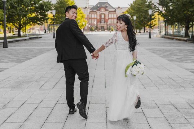 Vista traseira da noiva e do noivo caminhando pela rua de mãos dadas