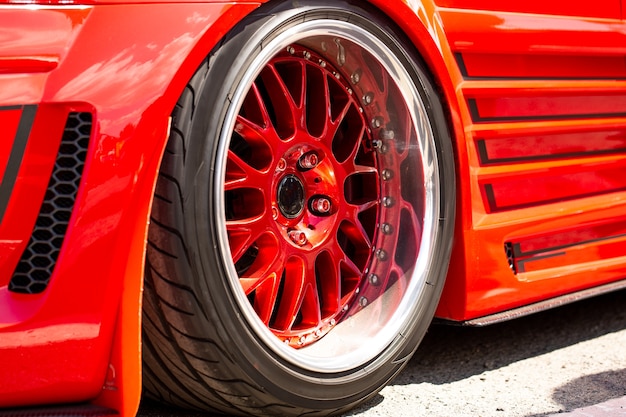 Vista traseira da roda, close-up do carro esportivo vermelho afinado. Dia do carro da moda na estrada