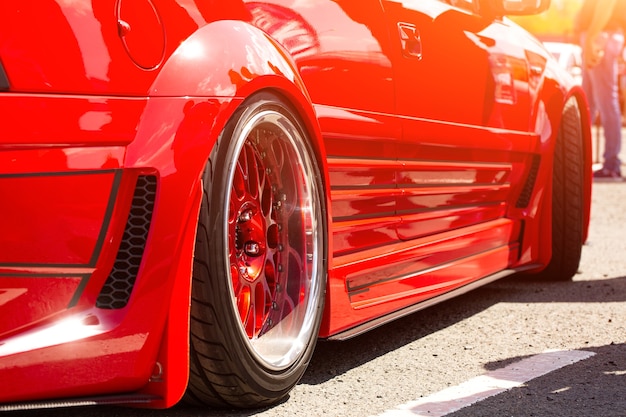 Vista traseira da roda, close-up do carro esportivo vermelho afinado. Dia do carro da moda na estrada