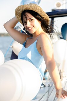 Vista traseira de alegre atraente mulher incrível no vestido azul e chapéu, desfrutando de água azul no convés de um iate à vela. conceito de regata à vela, férias de luxo no mar.