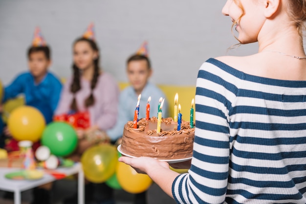 Vista traseira, de, menina, segurando, bolo aniversário chocolate, com, iluminado, vela, em, a, partido