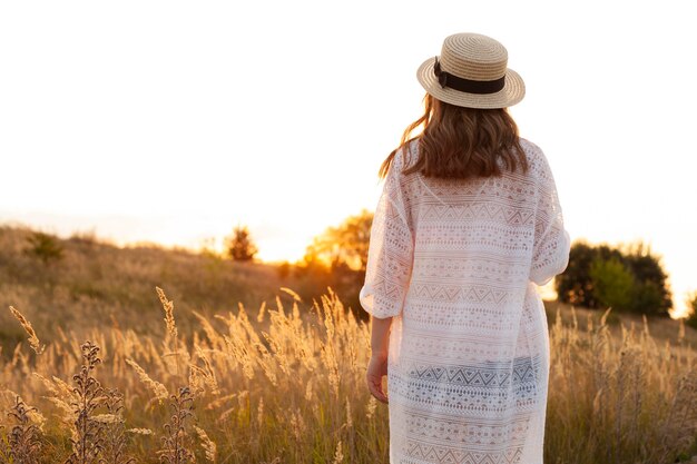 Vista traseira de mulher com chapéu posando no campo ao ar livre