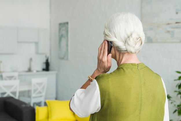 Vista traseira, de, mulher sênior, conversa num smartphone, casa