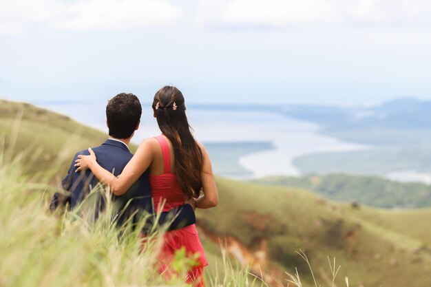 Vista traseira de um casal no dia do noivado, olhando para a bela paisagem