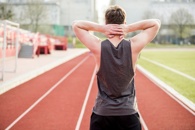 Vista traseira de um corredor masculino em pé na pista de corrida com as mãos atrás da cabeça