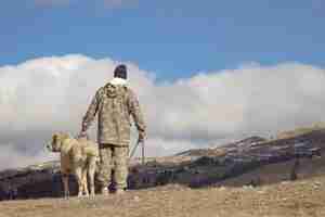 Foto grátis vista traseira de um homem com seu cachorro em uma colina alta apreciando a vista