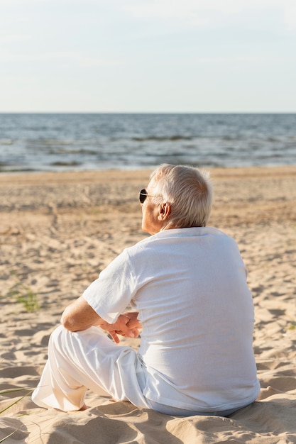 Vista traseira de um homem mais velho admirando a vista na praia enquanto descansava ao sol