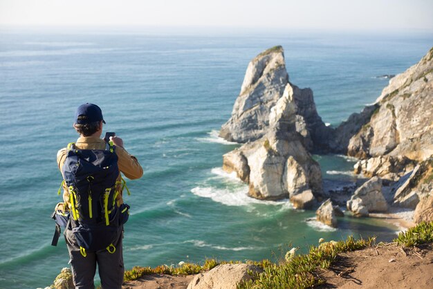 Vista traseira de um mochileiro tirando foto da paisagem marinha