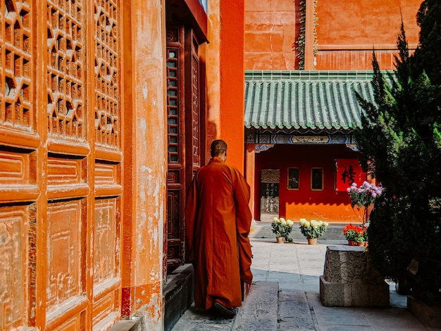 Vista traseira de um monge em um uniforme laranja caminhando perto de