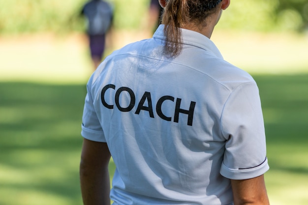 Vista traseira de um treinador de esporte feminino assistindo sua equipe competindo em um campo de esporte ao ar livre