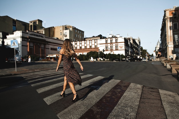 Vista traseira de uma garota de vestido no salto alto no cruzamento vazio nas ruas da cidade