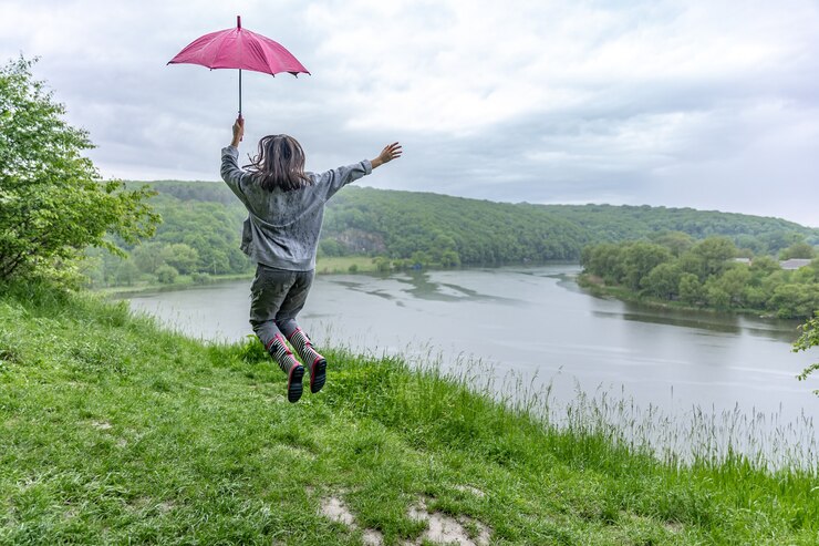Foto grátis vista traseira de uma garota sob um guarda-chuva, pulando perto de um lago em uma área montanhosa em tempo chuvoso.