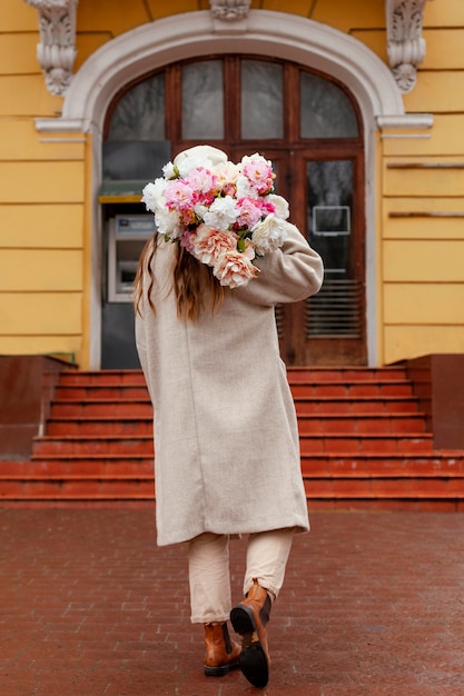 Foto grátis vista traseira de uma linda mulher segurando um buquê de flores do lado de fora