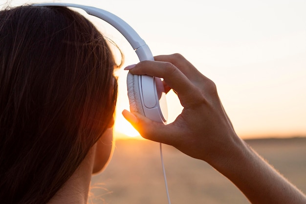 Vista traseira de uma mulher admirando o pôr do sol com fones de ouvido