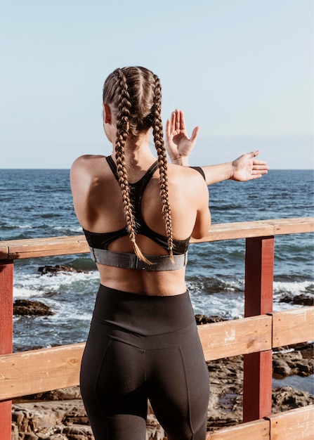 Vista traseira de uma mulher atlética ao ar livre na praia se espreguiçando enquanto admira a vista
