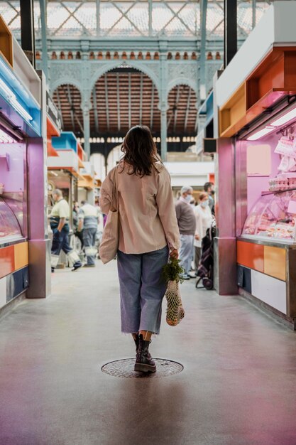 Vista traseira de uma mulher com sacolas de compras no mercado