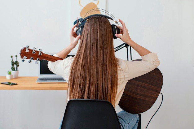 Vista traseira de uma musicista usando fones de ouvido para gravar música e tocar violão