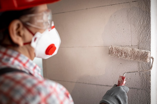 Vista traseira de uma trabalhadora da construção civil com capacete e rolo de pintura