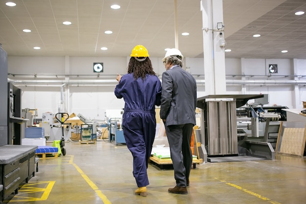 Foto grátis vista traseira do chefe em pé na fábrica e ouvindo o trabalhador da fábrica