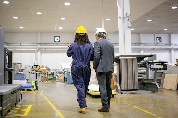 Vista traseira do chefe em pé na fábrica e ouvindo o trabalhador da fábrica