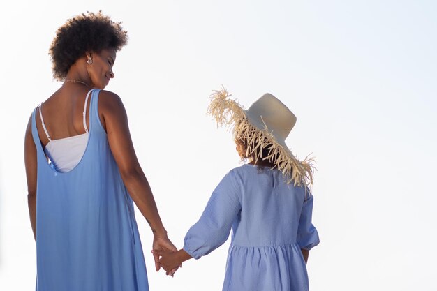 Vista traseira do concurso mãe e filha de mãos dadas na praia. Família afro-americana a passar tempo juntos ao ar livre. Lazer, tempo em família, conceito de união