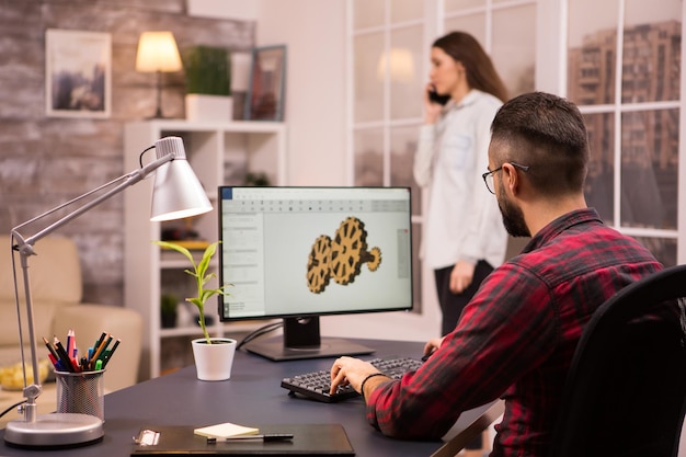 Vista traseira do engenheiro masculino desenhando um protótipo mecânico usando software CAD na sala de estar. Namorada em segundo plano.