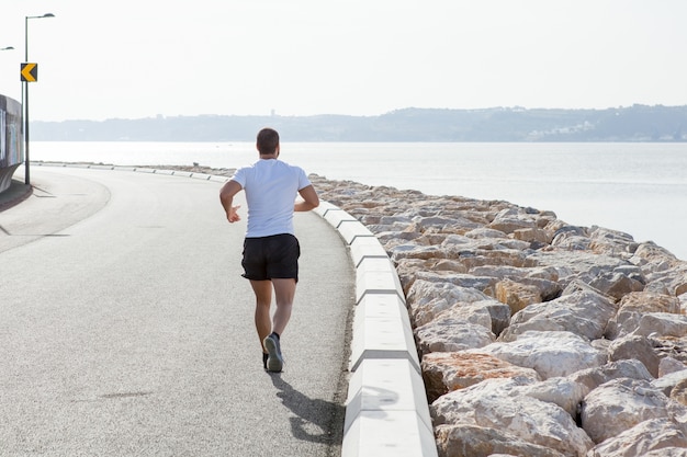 Foto grátis vista traseira do homem forte que corre na estrada do beira-mar