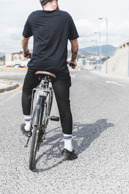 Vista traseira do homem sentado na bicicleta ao longo da estrada reta