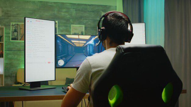 Vista traseira do jogador profissional fazendo streaming de sua competição em configuração de monitor triplo com dois chats de streaming abertos