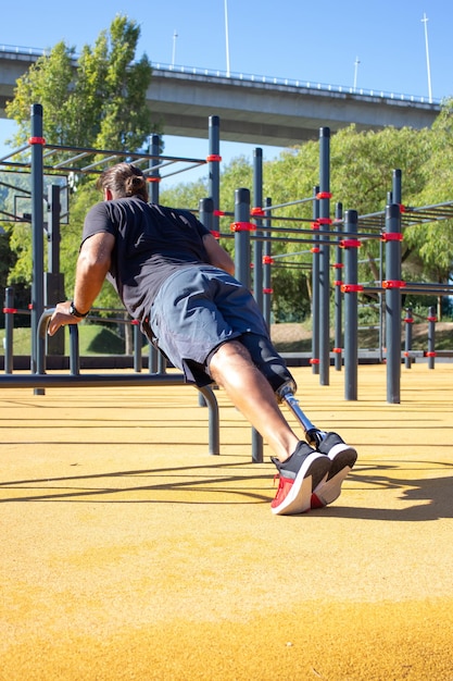 Vista traseira do jovem com perna protética fazendo flexões. homem desportivo fazendo esportes nas mãos de treinamento do estádio, apoiando-se na barra sobre o chão. motivação para a vida ativa para pessoas com conceito de deficiência