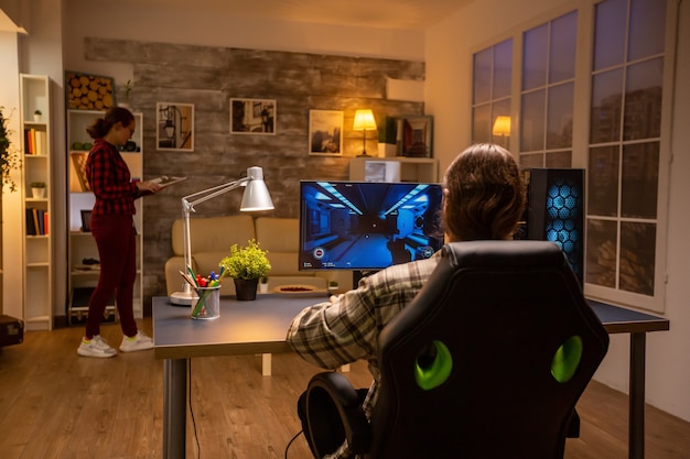 Vista traseira do videogame profissional jogando em um PC poderoso tarde da noite na sala de estar.