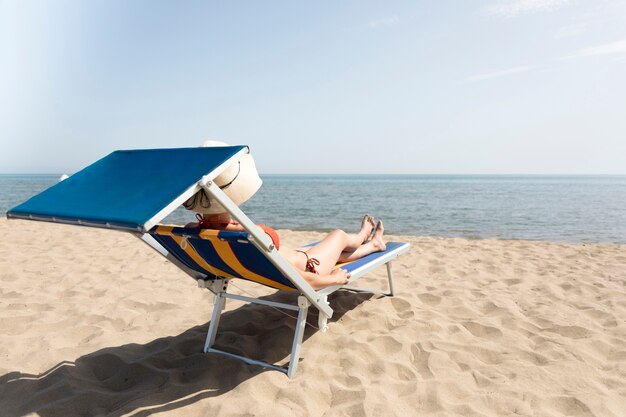 Vista traseira, mulher, ligado, cadeira praia, sunbathing