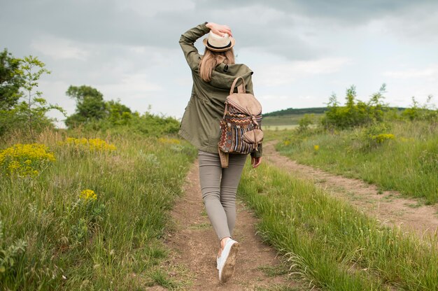 Vista traseira viajante com chapéu caminhando ao ar livre