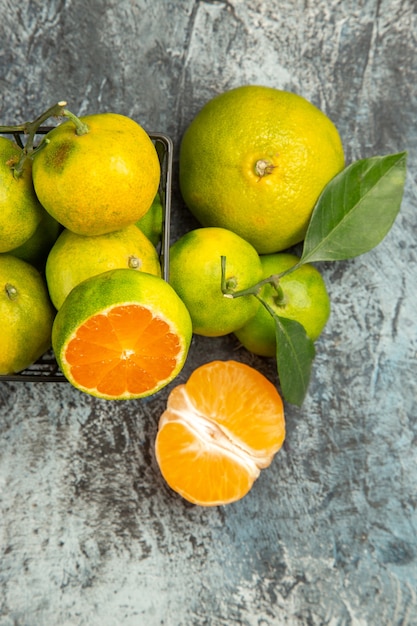 Vista vertical da cesta com tangerinas verdes frescas cortadas ao meio e tangerina descascada em fundo cinza