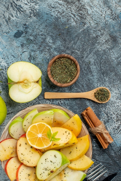 Vista vertical da coleção de frutas orgânicas frescas em um prato branco Talheres de limão e canela em uma mesa escura