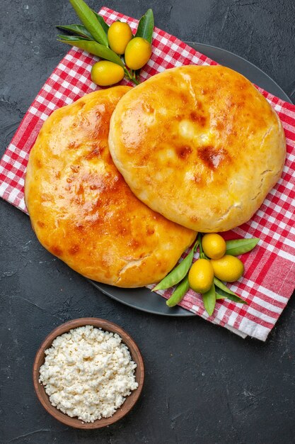 Vista vertical de deliciosos kumquats de pastelaria acabada de fazer com o caule numa toalha vermelha despojada e queijo no fundo escuro