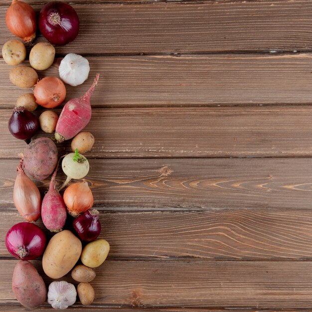 Vista vertical de legumes como batata de alho de cebola rabanete em fundo de madeira com espaço de cópia